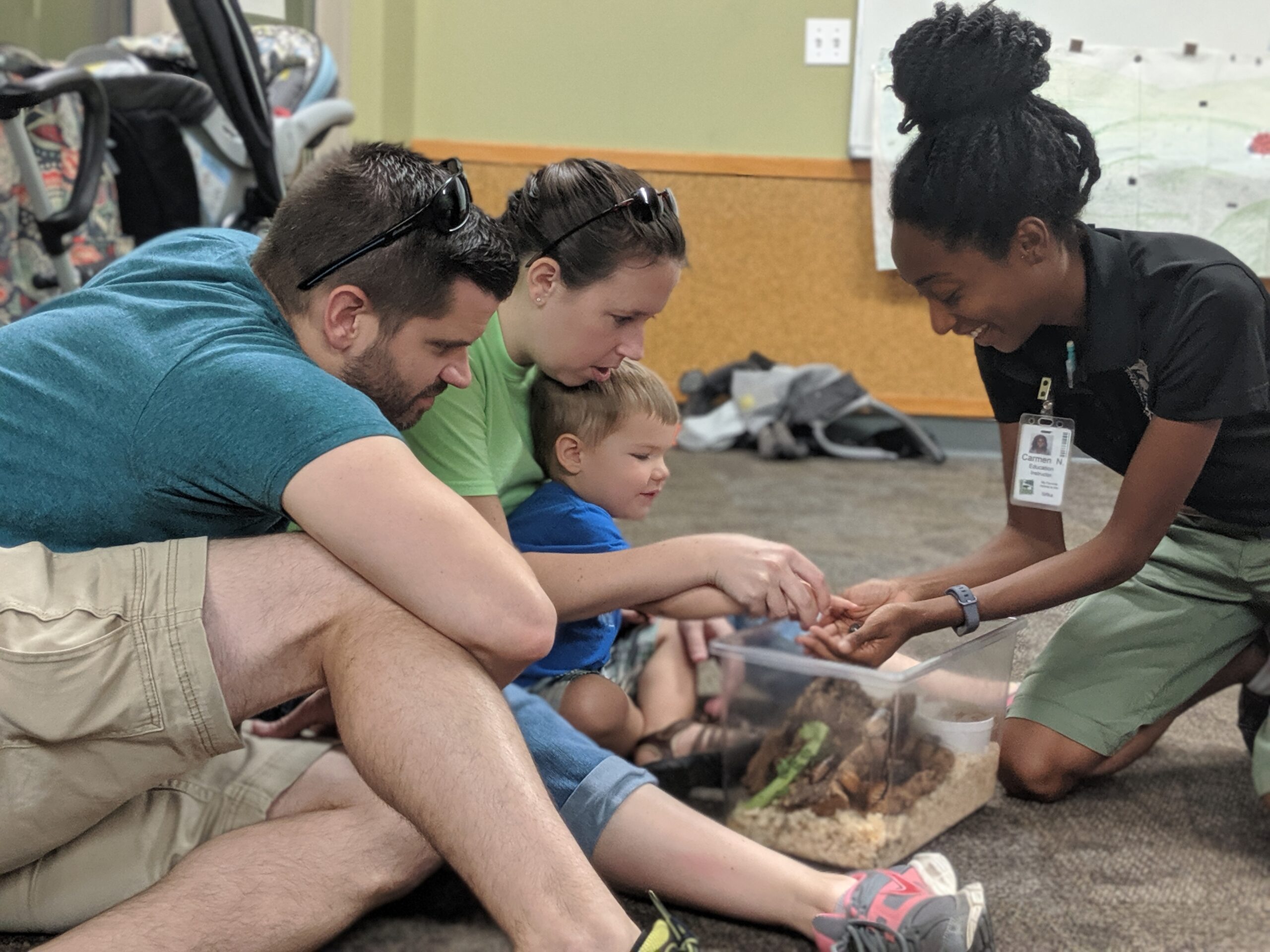 two adults and small child touching a cockroach held by educator