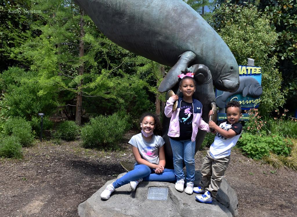 three children posing near a statue of a manatee